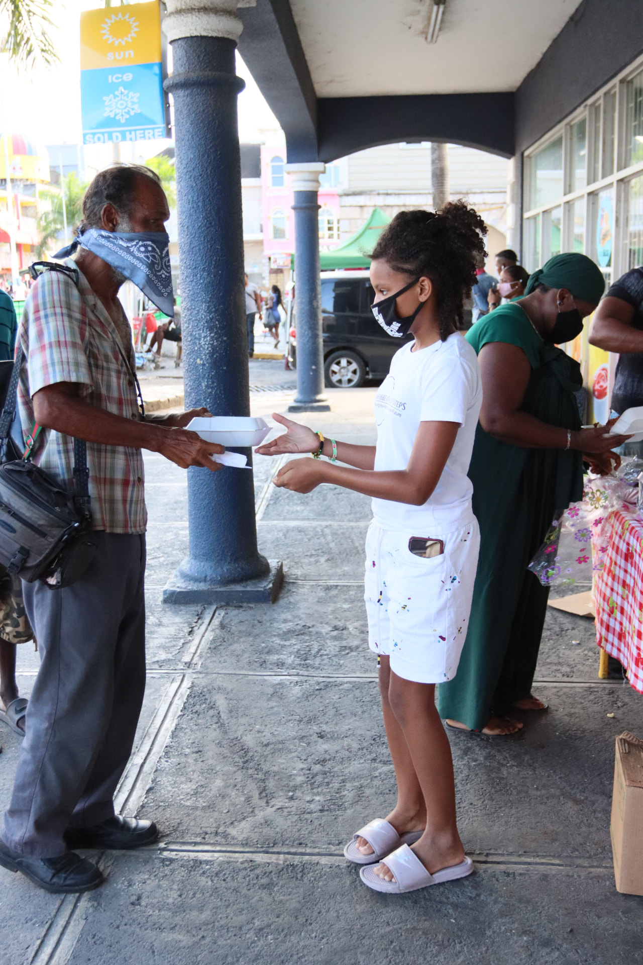 A Mrs. B’s Table volunteer hands a meal directly to a gentleman outside a storefront.