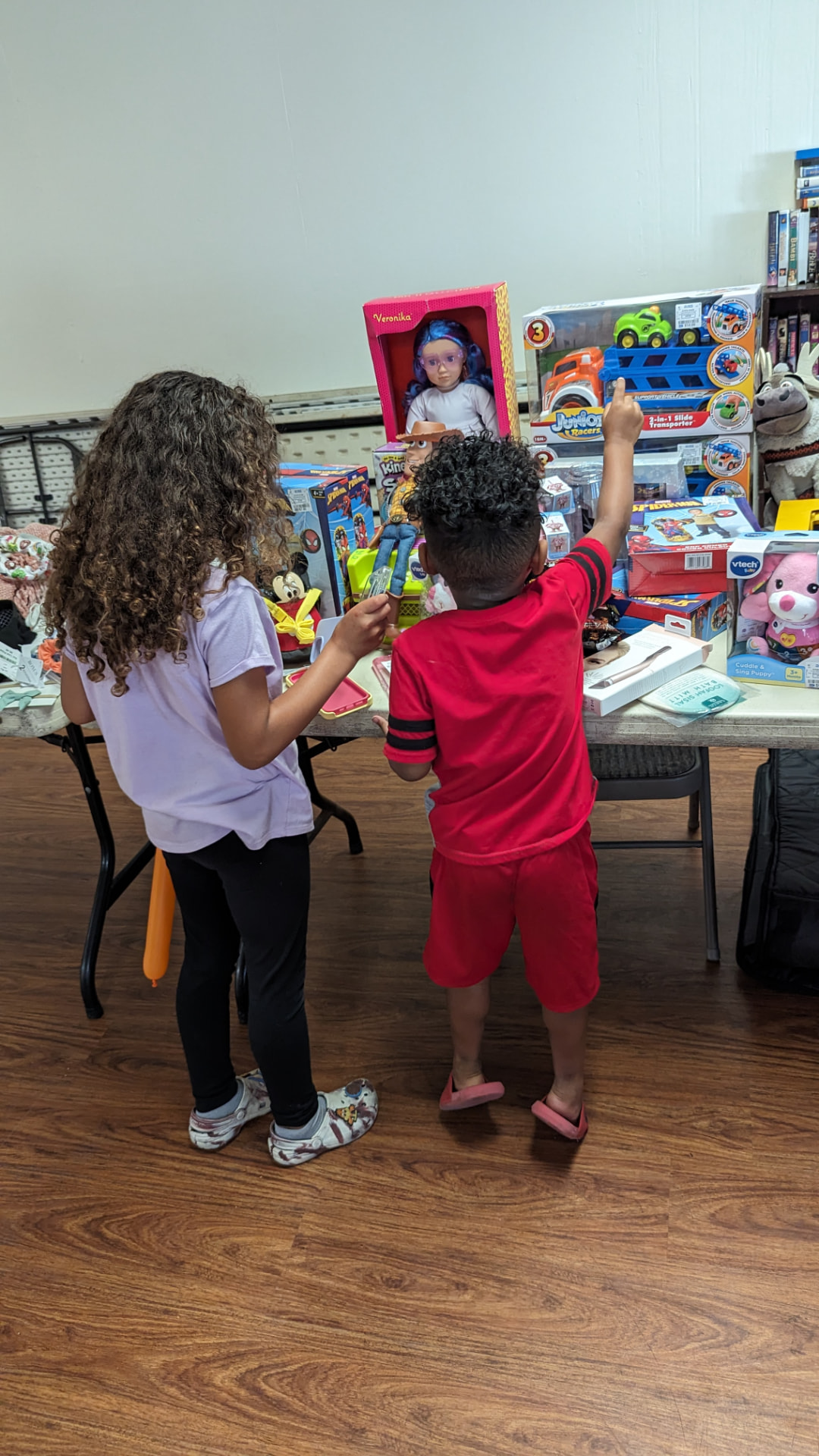 Two children select toys from a table at Mrs. B’s Toy Shoppe.
